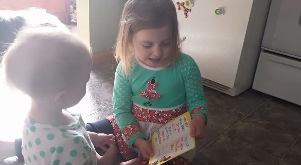 Older sister reading a book to baby sister