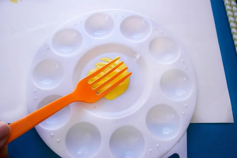 Fork in yellow paint in middle of small white paint palette.