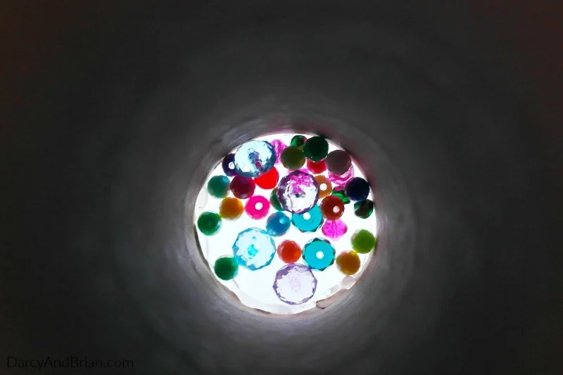 Inside view of colorful plastic beads inside paper tube used to make a kaleidscope craft.