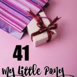 Present wrapped in light pink paper and red bow coming out of a pink and purple striped gift bag on a pink background.