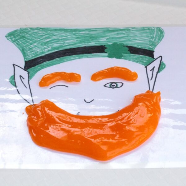 Laminated hand drawn leprechaun face with green hat with orange slime eyebrows and beard.