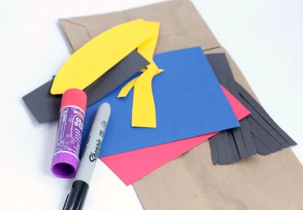 Brown paper bag, yellow, blue, red, and black construction paper, Sharpie marker, and glue stick.