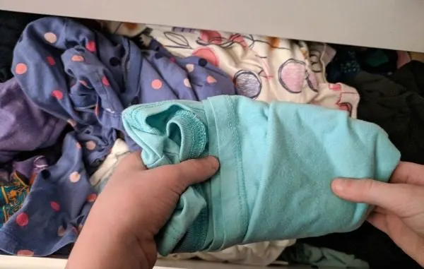 Child putting away clothes in dresser drawer.