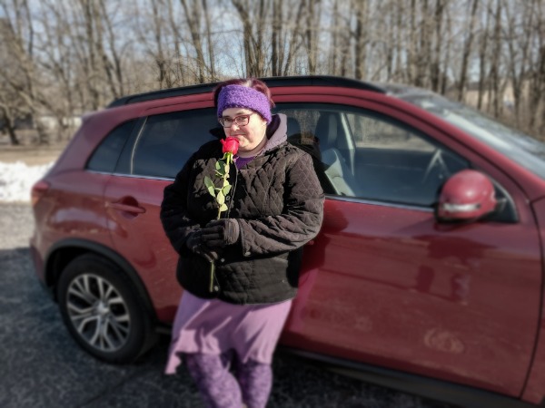 Darcy leaning against the 2018 Mitsubishi Outlander and holding a rose.