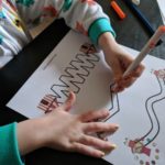 Preschooler practicing early writing skills by tracing lines on circus printable worksheet.