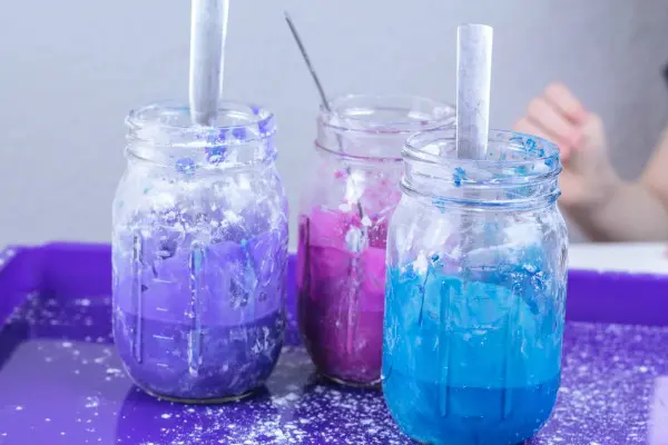 Three mason jars sitting in purple activity tray. One jar has purple oobleck, another has pink and the third has blue.