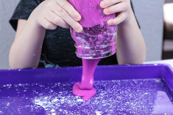 Child pouring thick pink gooey substance out of mason jar.