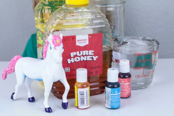 Supplies needed for making a unicorn density tower. Includes water, honey, vegetable oil, food coloring, and unicorn toy.