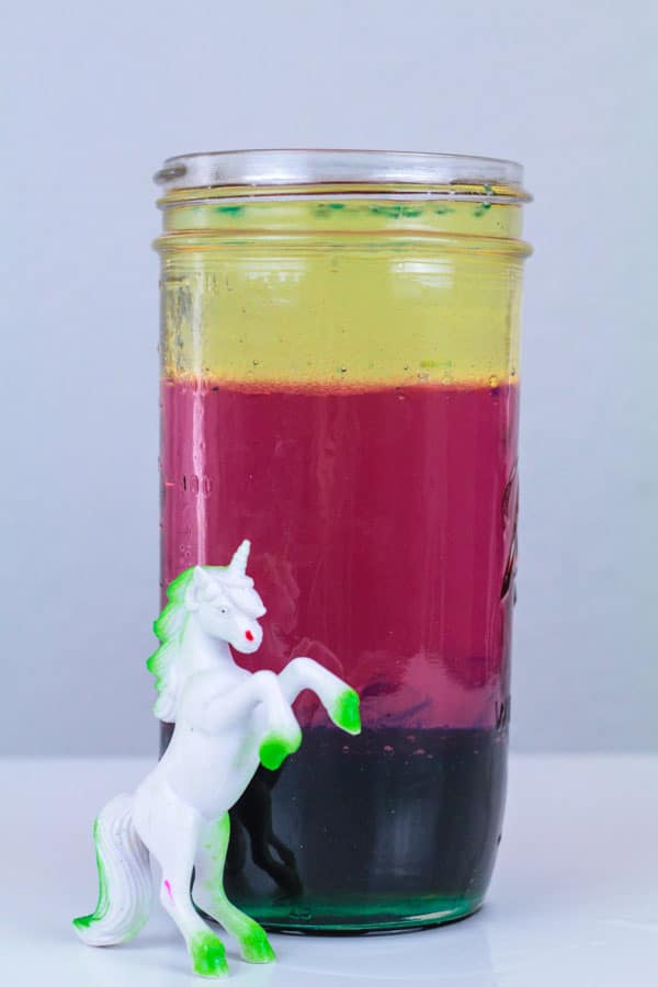 Density tower jar filled with blue, pink, and yellow layers. Unicorn toy stands next to the jar.