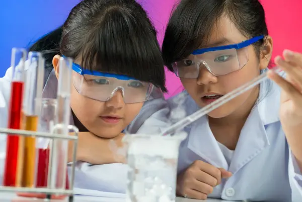 Two young Asian girls wearing safety glasses and doing science experiments