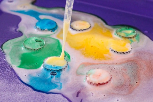 Squeezing vinegar onto bottle caps with pipette for kids science activity.