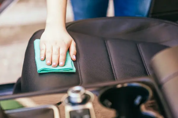 Woman wiping off front seat in car.