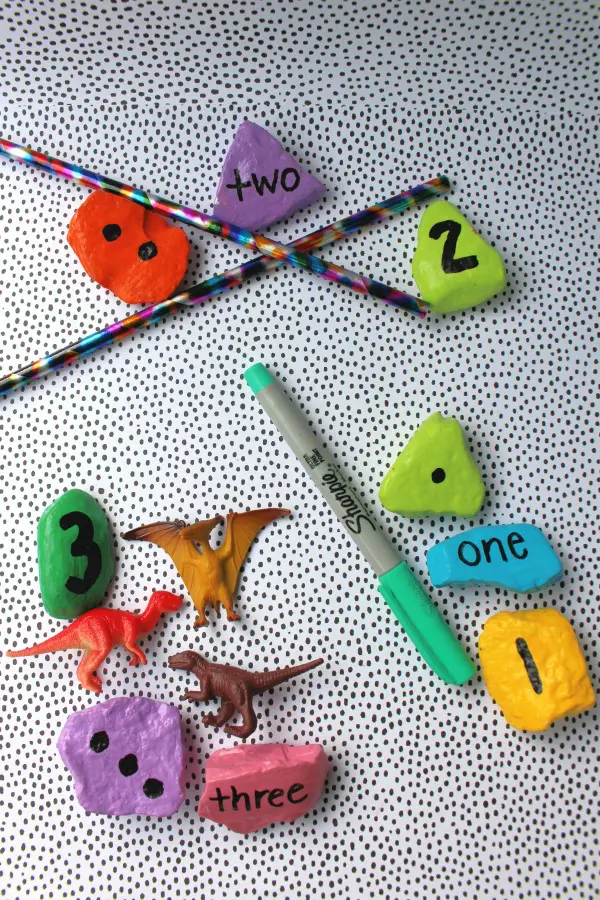 Number rocks with matching amount of pencils, sharpie marker, and dinosaur toys.
