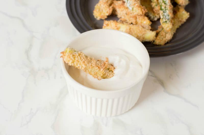 One zucchini fry dipped in sauce in small white ramekin