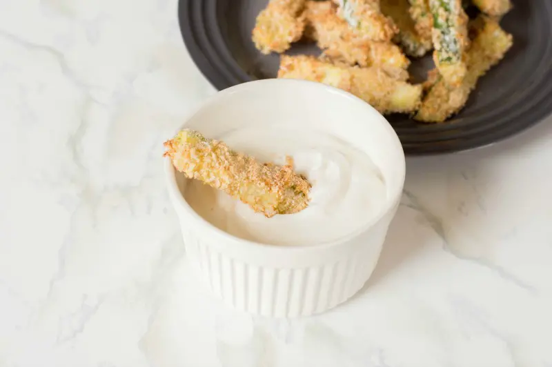 One zucchini fry dipped in sauce in small white ramekin