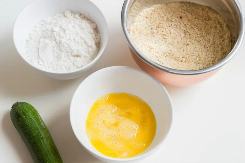 Three bowls on counter. One with flour, one with whisked eggs, and one with bread crumbs