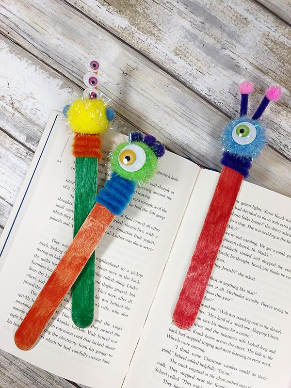 Finished yellow, green, and blue monster craft stick bookmarks laying on a book.