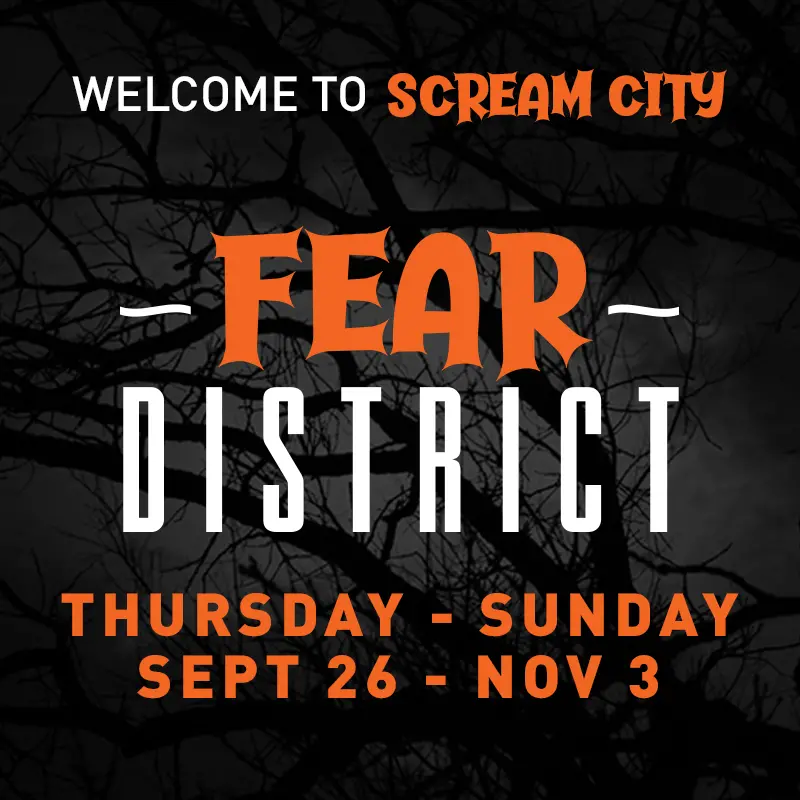 Orange and white text with dates for Fear District event with a dark background with a silhouette of tree branches