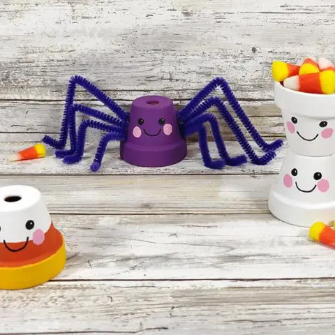 Finished Kawaii Halloween flower pots. One painted in candy corn colors, a purple spider, and two ghosts stacked on top of each other. All have cute Kawaii inspired faces.