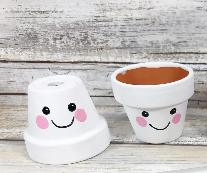 One upside down mini flower pot and one flower pot standing right side up. Both painted white with cute smiley faces.