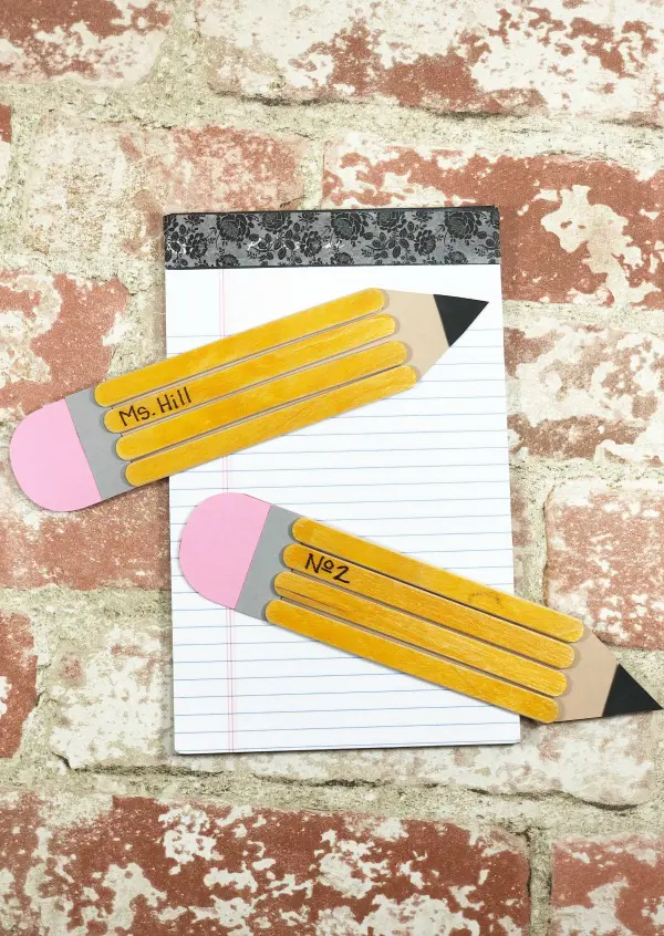 Two school pencils made with paper and wooden craft sticks on notebook with brick background