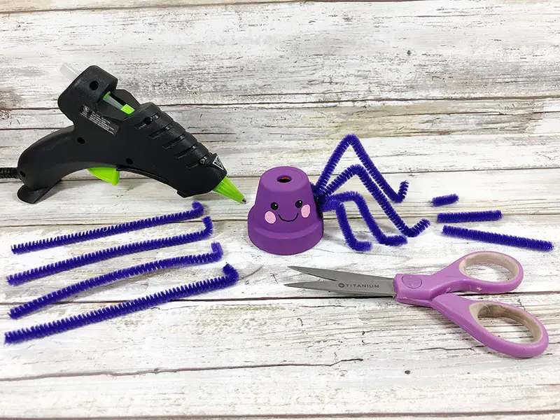 Attaching purple pipe cleaners to flower pot with glue gun.
