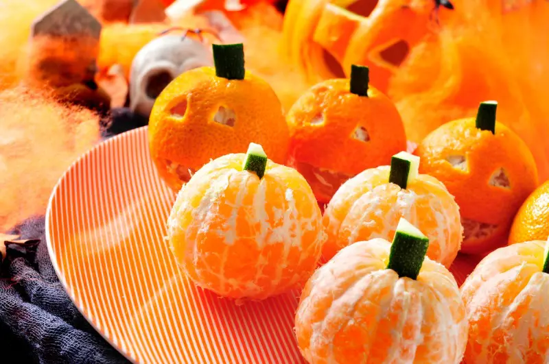 Tangerines decorated like pumpkins on orange plate