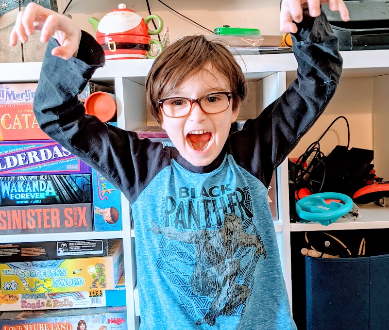 Caucasian boy wearing a blue long sleeve shirt with arms raised and mouth open roaring like a lion.