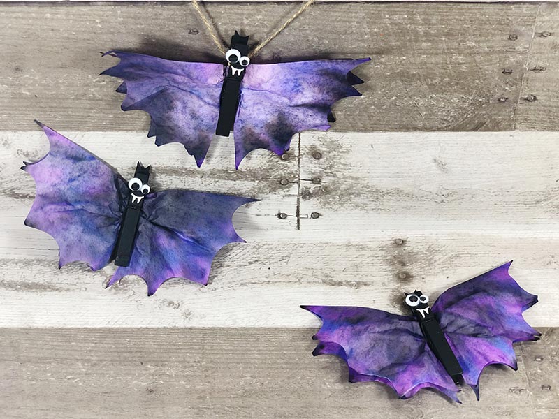 Three finished coffee filter bats laying on gray wood photo backdrop