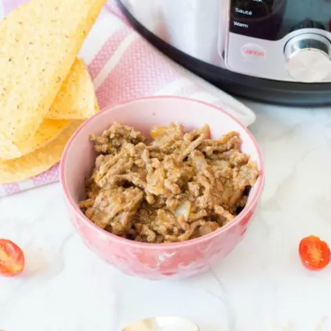 Cooked taco meat in pink bowl on counter by taco shells, tomatoes, and Instant Pot