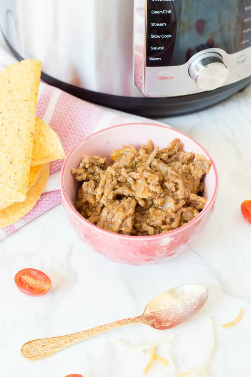 Taco meat in pink bowl on counter next to spoon, shells, and pressure cooker