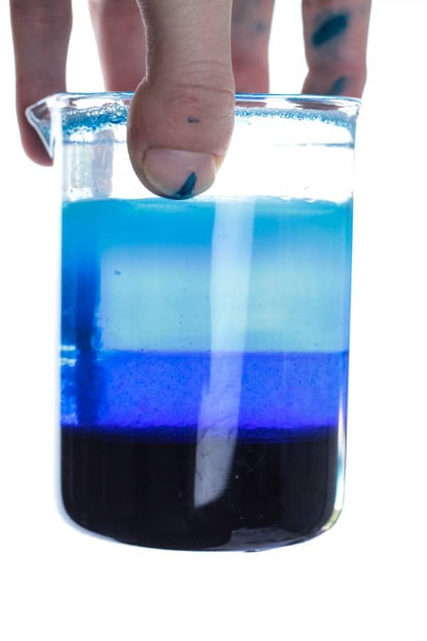 Hand holding completed ocean zone density jar showing different shades of blue layers