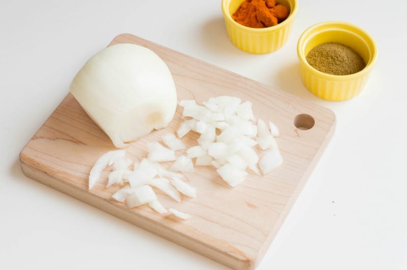 Partially chopped onion on cutting board and seasonings in small yellow ramekins