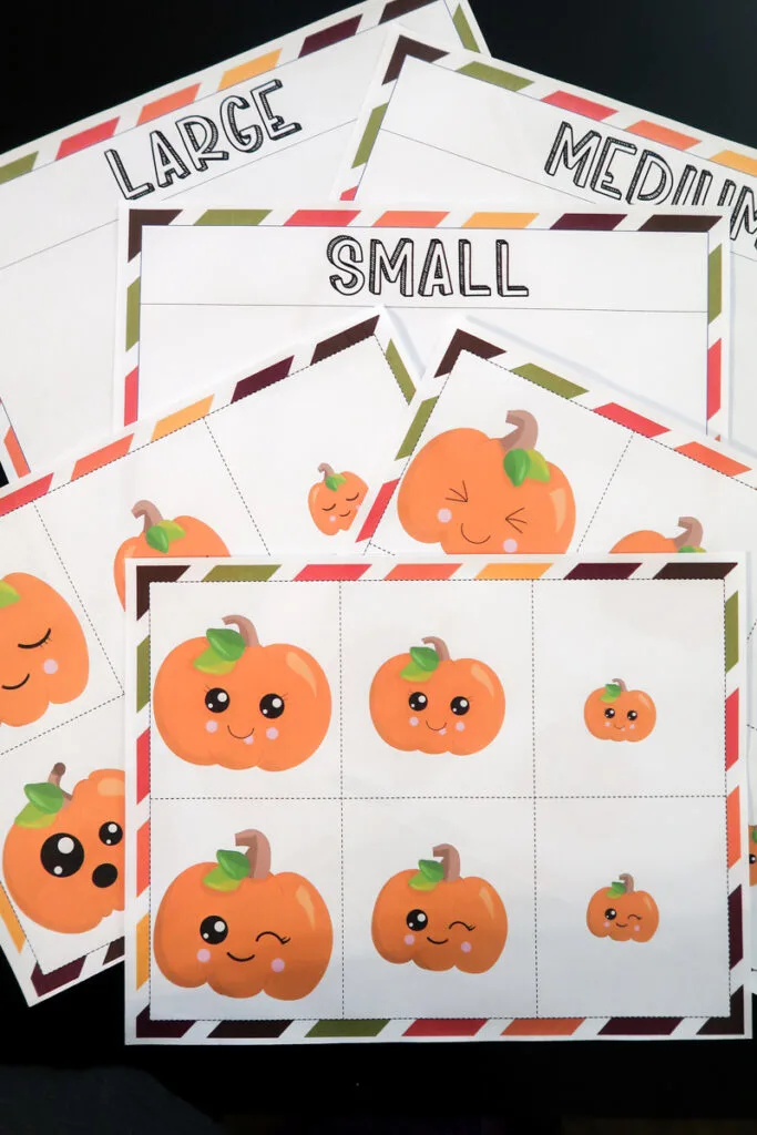 Pumpkin size sort activity pages printed out and fanned out on a black tabletop.