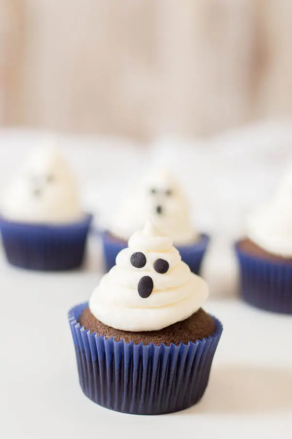 Chocolate cupcake in blue wrapper with marshmallow frosting ghost face. Cupcakes sitting on a white tablecloth