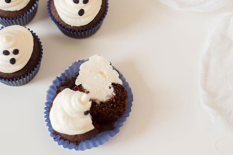 Completed chocolate marshmallow ghost cupcakes and one split open on a white background.