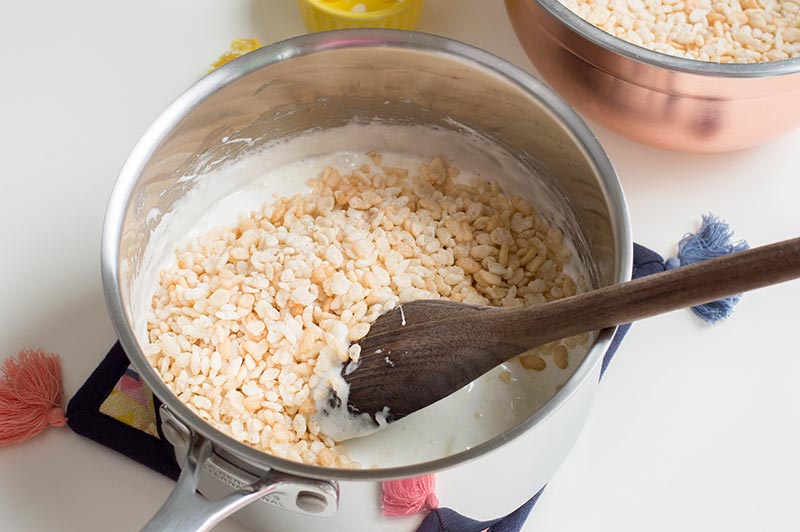 Mixing rice krispie cereal into melted butter and marshmallow mixture in silver saucepan