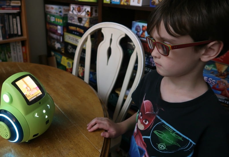 Boy standing next to table, looking at Miko 2 robot and listening to a story.