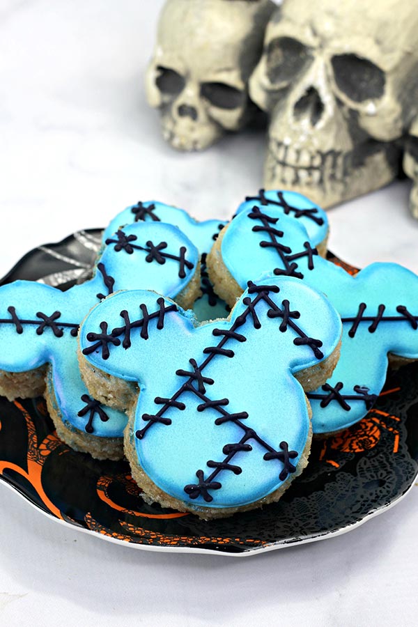 Plate of Sally inspired rice crispy treats shaped like Mickey. Black and orange plate on white background and skull decorations.