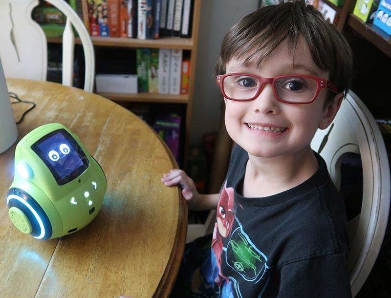 6 year old boy (author's son) smiling and sitting at a table with a green Miko 2 robot.