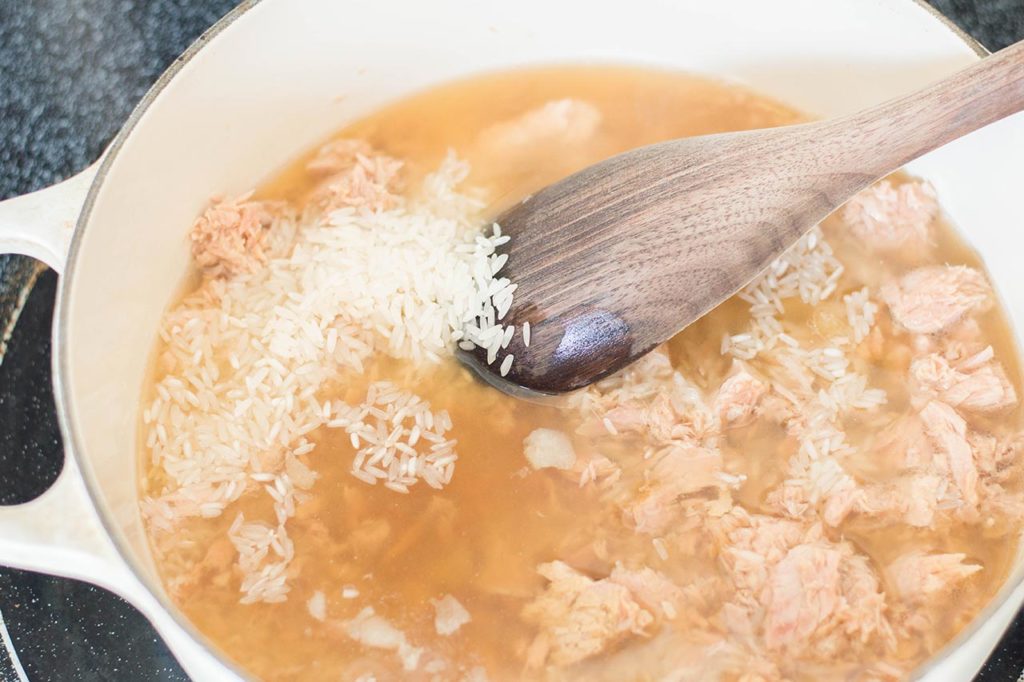 Wooden spoon stirring tuna and rice in broth.