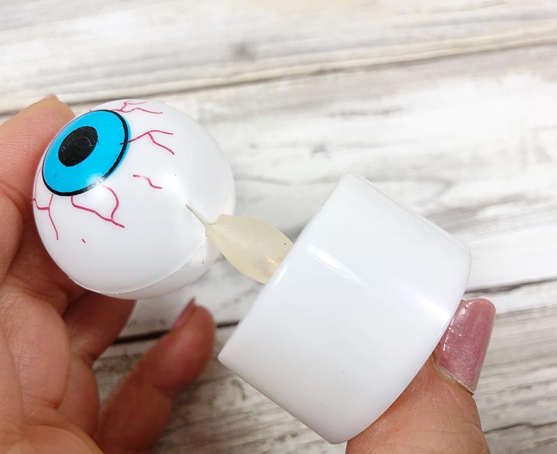 Woman's hand holding blue plastic eyeball and inserting tea light candle into bottom
