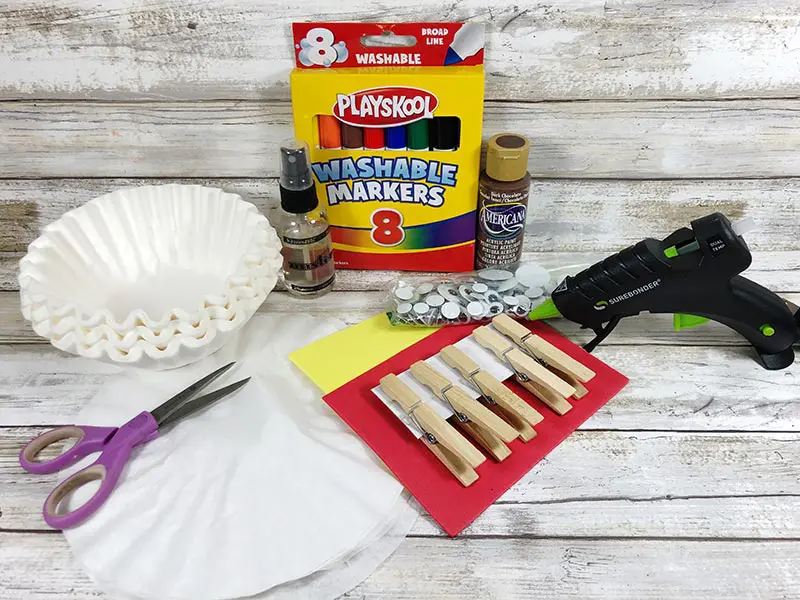 Coffee filters, clothespins, googly eyes, markers, and other craft supplies on white wood background.
