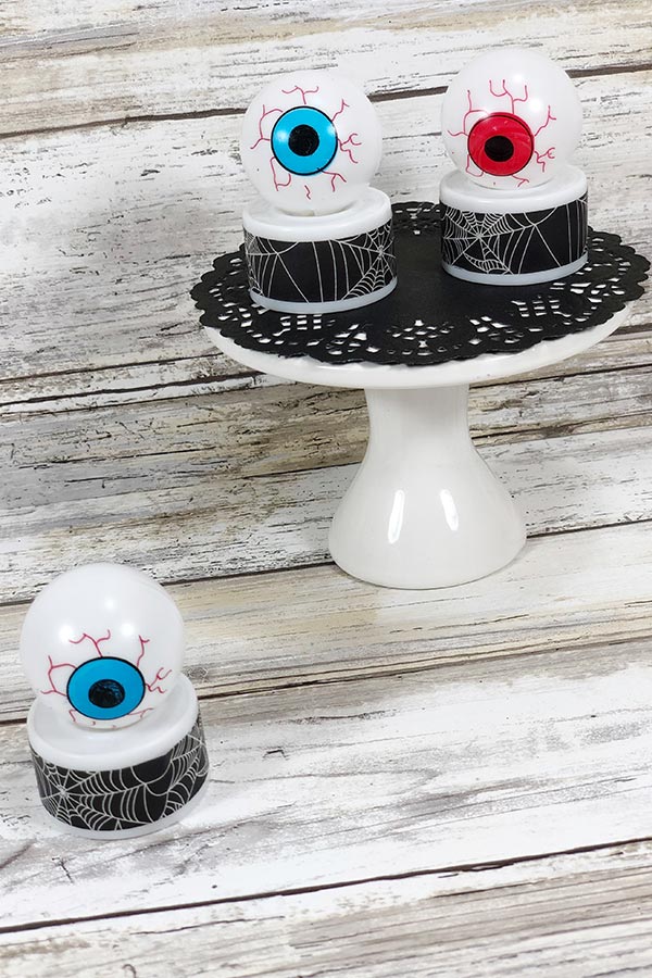 Two completed eyeball tea lights on white cake pedestal with black doily. One blue eyeball light on table next to pedestal