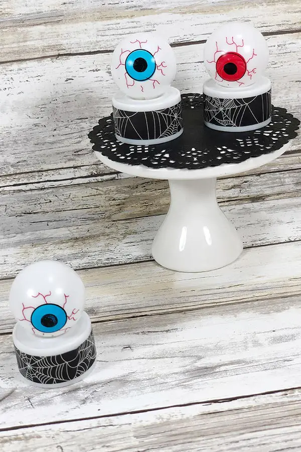 Two completed eyeball tea lights on white cake pedestal with black doily. One blue eyeball light on table next to pedestal