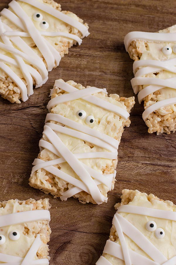 Completed mummy rice crispy treats laying on brown wooden table.