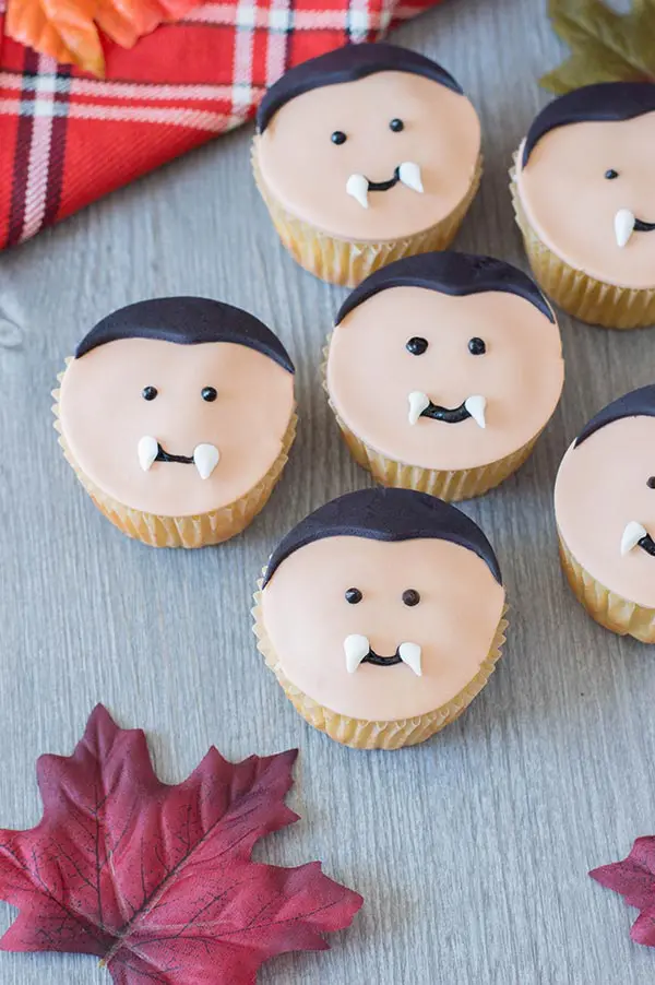 Five completed vampire cupcakes on gray table with decorative red plaid napkin and fake red leaves.