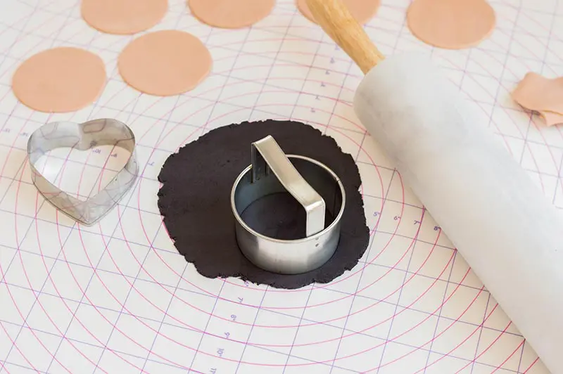 Circle cookie cutter cutting out beige and black fondant circles on pastry mat.