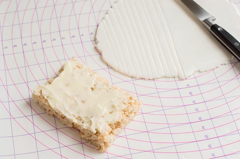 Frosted rice crispy treat on pastry mat next to rolled out white fondant.