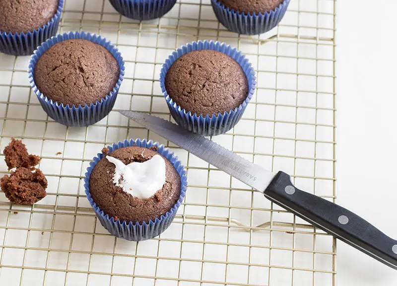 Chocolate cupcakes on wire cooling rack. One has marshmallow fluff filling added.